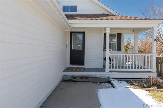 White house entry with a black front door, covered porch, and snow along the walkway.