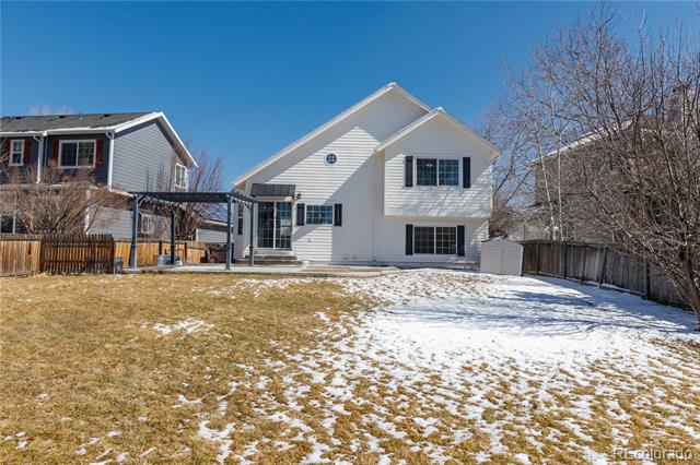 White two-story home viewed from its fenced backyard, with a covered patio and patchy snow.