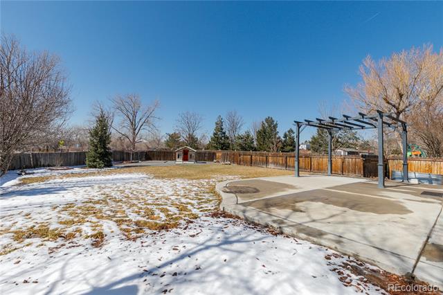 Snow-dusted backyard with a concrete patio and black pergola.