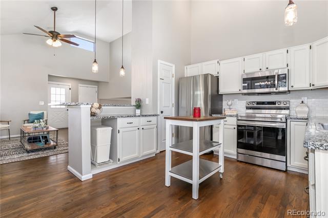 Open-plan kitchen with white cabinetry, stainless steel appliances, and a rolling island.