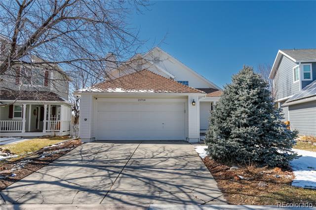 Light-colored home with a two-car garage, broad driveway, and large evergreen tree beside it.