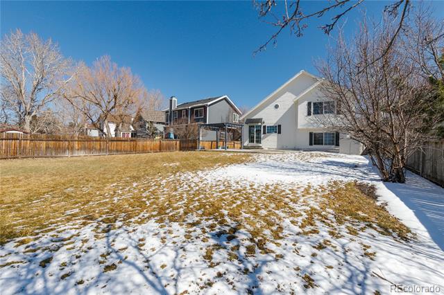 House rear and fenced backyard with patchy snow and leafless trees.