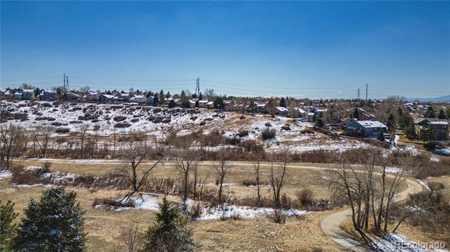Panoramic view of snow-dusted open space with a winding path and homes along the ridge.