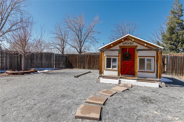 Gravel backyard with a fenced perimeter, small wooden outbuilding with a red door, and stepping-stone path.