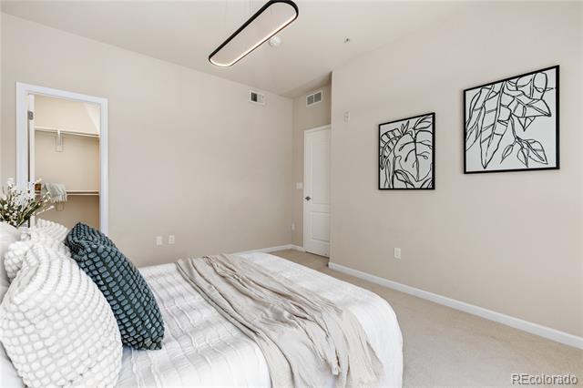 Furnished bedroom with white and gray bedding and framed botanical prints.