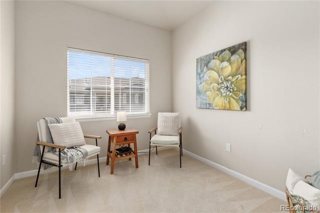 Staged sitting area with two chairs, a wooden table, window blinds, and floral wall art.