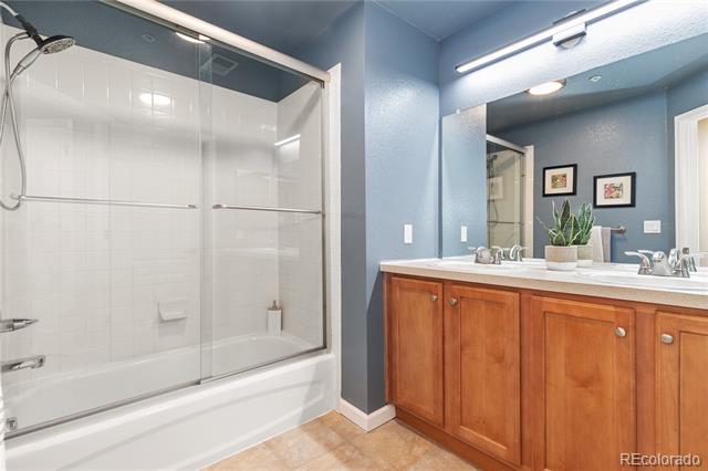 Bathroom with a glass-enclosed tub and long wood vanity against blue walls.