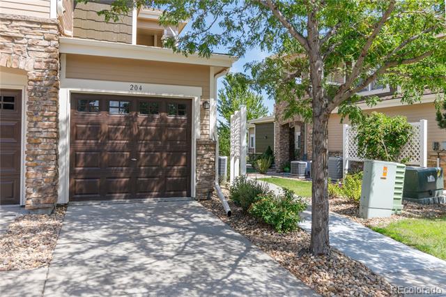 Townhome exterior with a stone-accented facade, dark garage door marked 204, and leafy tree.