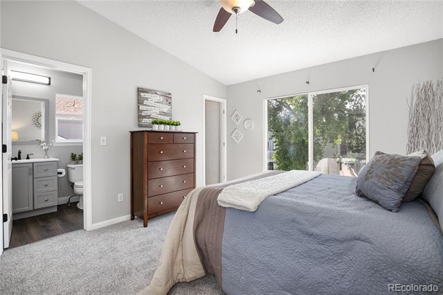 Bedroom with gray bedding, wooden dresser, and a large window overlooking trees; bathroom visible through doorway.