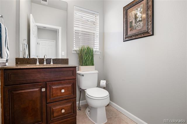 Bathroom with a dark wood vanity, granite countertop, and toilet beneath a window with blinds.