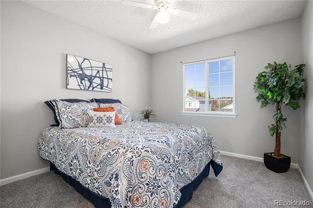 Staged bedroom with a patterned bedspread, abstract wall art, a sunny window, and a potted tree.