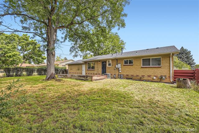Single-story brick house viewed from a grassy backyard beneath a large shade tree.
