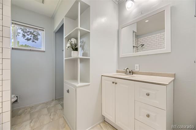 Bathroom with a white vanity, built-in shelving, tiled shower area, and window.