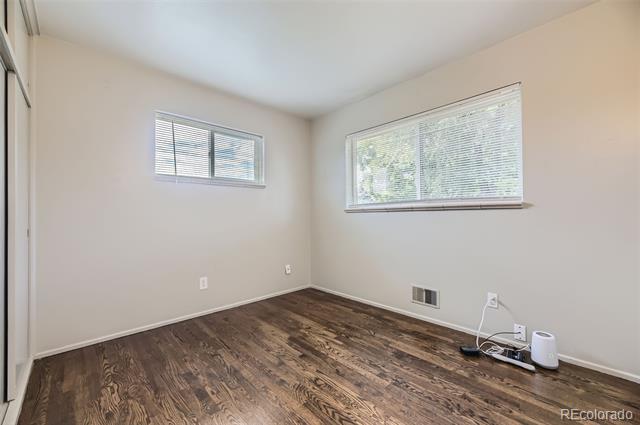 Empty bedroom with dark wood flooring, two windows with blinds, and a closet.