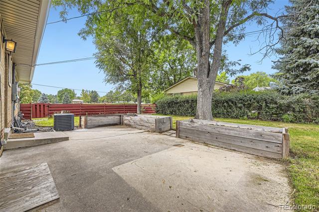 Backyard patio with raised wooden beds around a mature tree and a red fence.