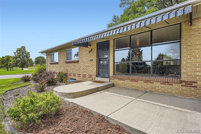 Brick home entrance with a metal awning, large windows, and a curved concrete walkway.