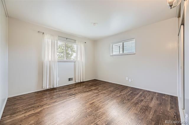 Empty room with dark wood floors, a large curtained window, and a smaller high window.