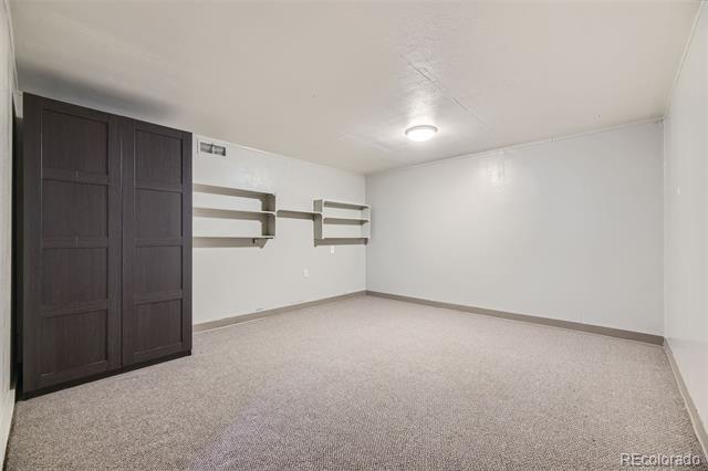 Empty carpeted room with dark sliding closet doors and wall-mounted shelves.