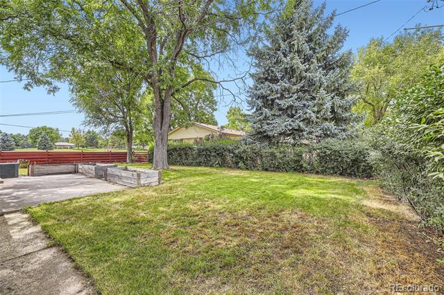 Backyard lawn with mature trees, a concrete patio, raised planter, and red fence.