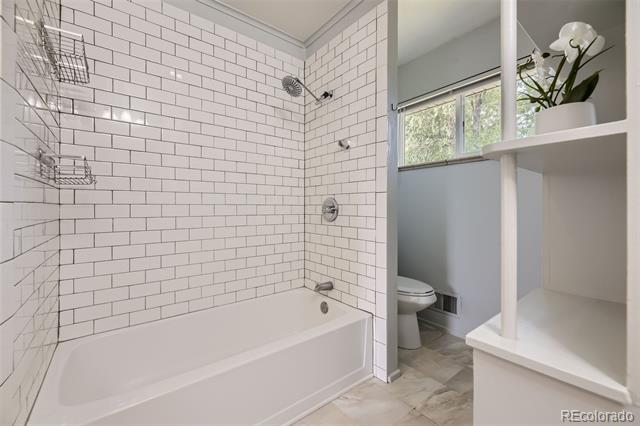 Bathroom with a white tub, tiled shower walls, and open shelving beside a window.