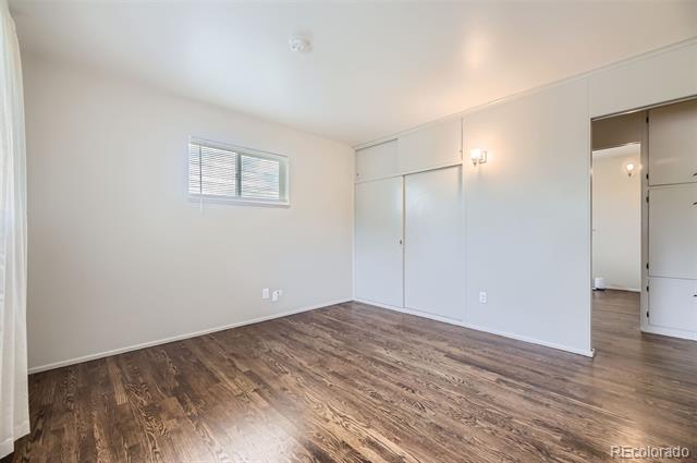 Empty bedroom with dark wood-look flooring, sliding closet doors, and a small window with blinds.