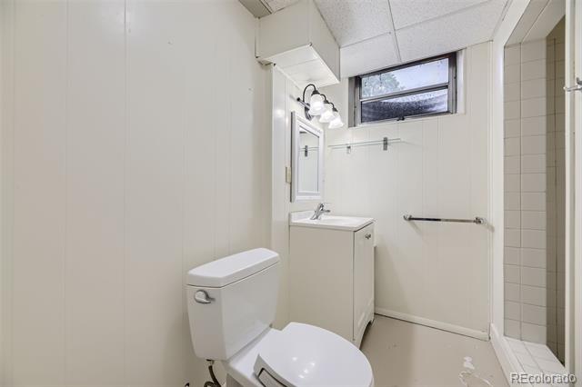Small bathroom with a white toilet, compact vanity, high window, and tiled shower alcove.