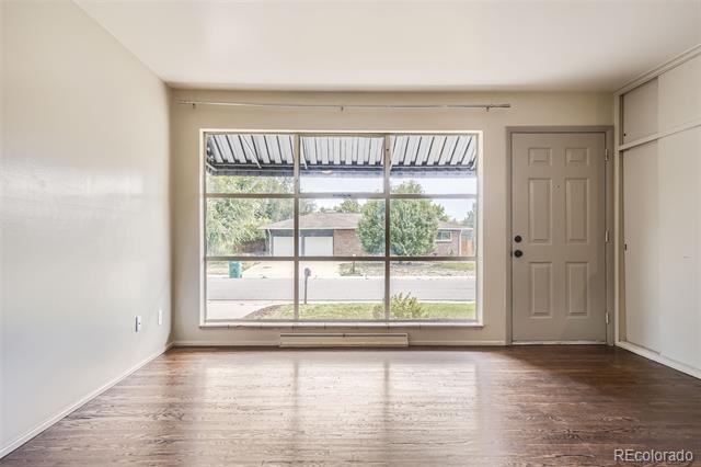 Vacant living room with hardwood floors, a large front window, and the entry door.