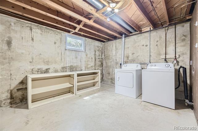 Basement laundry room with a washer and dryer beside open shelving and exposed ceiling joists.