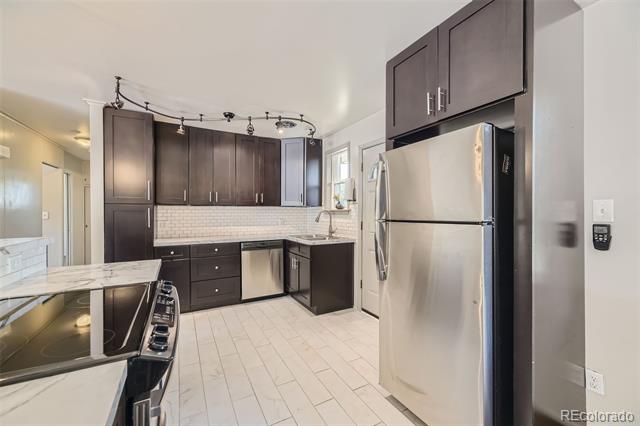 Kitchen with dark cabinets, stainless steel appliances, tile backsplash, and a cooktop breakfast bar.