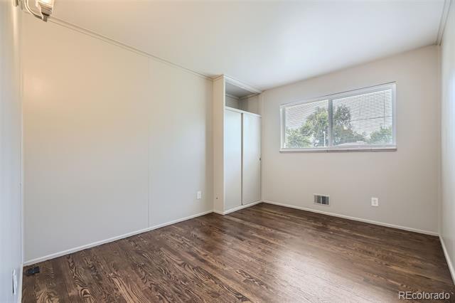 Empty bedroom with dark wood floors, a closet, and a window with blinds.