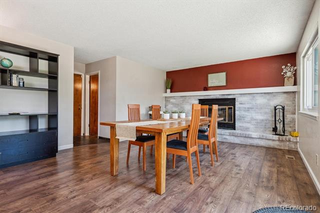 Dining area with a wooden table and chairs beside a stone-surround fireplace and red accent wall.