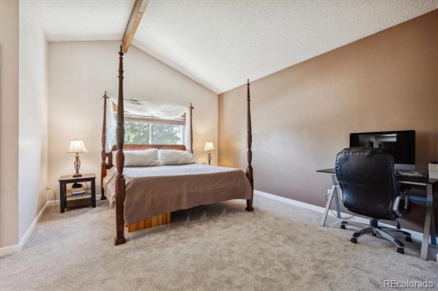 Bedroom with a four-poster bed, beige carpet, and a desk and office chair.