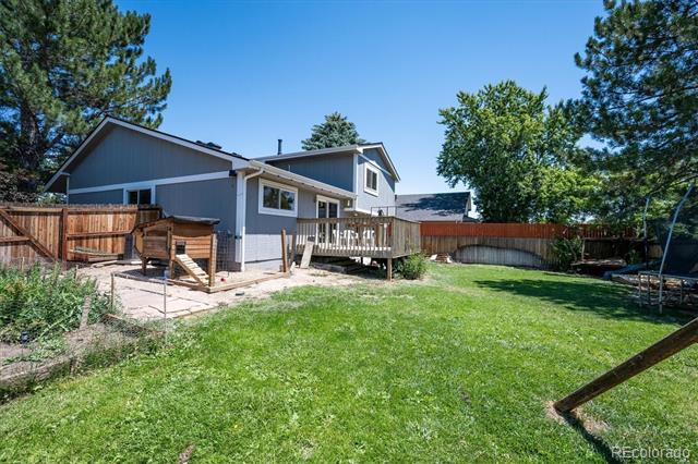 Gray home’s rear deck overlooks a fenced backyard with a broad green lawn and mature trees.