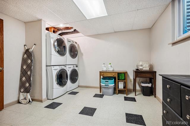 Laundry room with stacked front-loading machines, an ironing board, and black accent tiles in the floor.