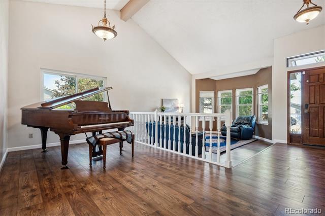 Vaulted entry with a dark wood grand piano, hardwood floors, and a white railing beside the seating area.