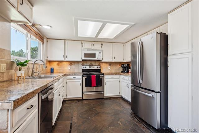 Kitchen with white cabinets, granite countertops, stainless steel appliances, and a window over the sink.