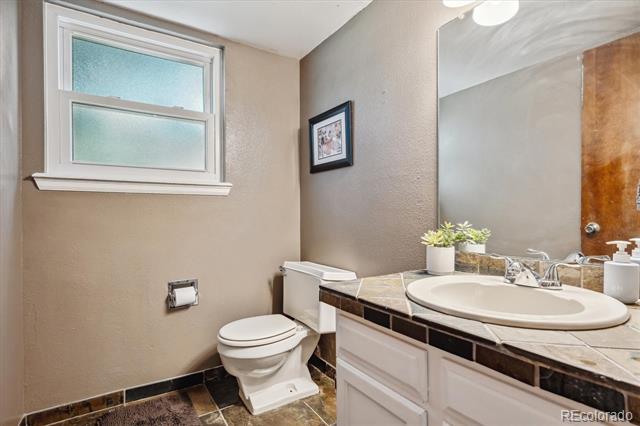 Bathroom with a white vanity, dark tile countertop, large mirror, and high window.