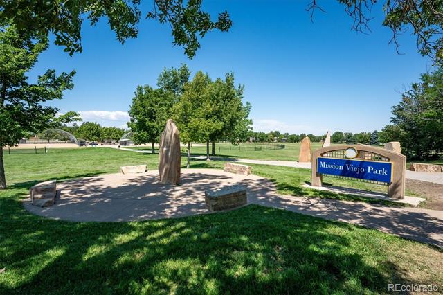 Mission Viejo Park sign beside a shaded stone seating area and open green parkland.
