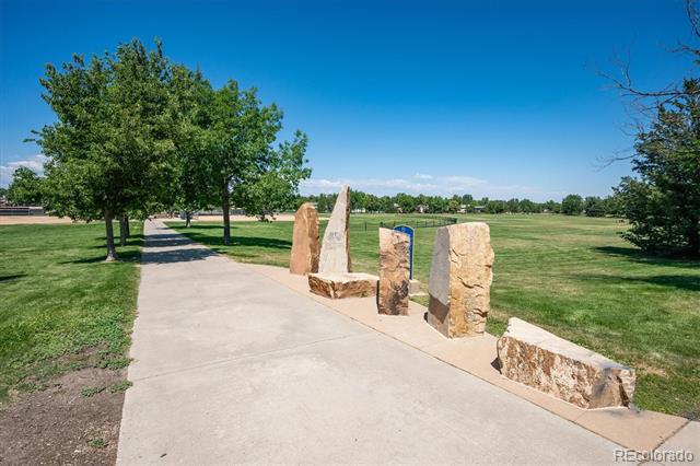 Paved park path beside grassy fields and trees, lined with upright stone markers.