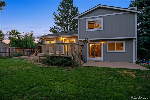 Gray two-story house with a raised wooden deck and broad lawn at dusk.