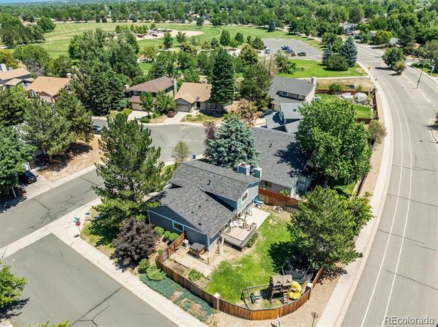 Aerial view of a gray-roofed home with a fenced yard on a leafy neighborhood corner.