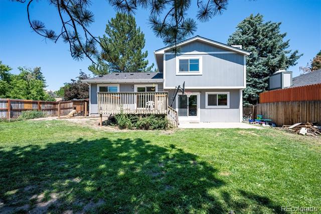 Rear of a two-story gray house with a raised deck and broad fenced lawn.