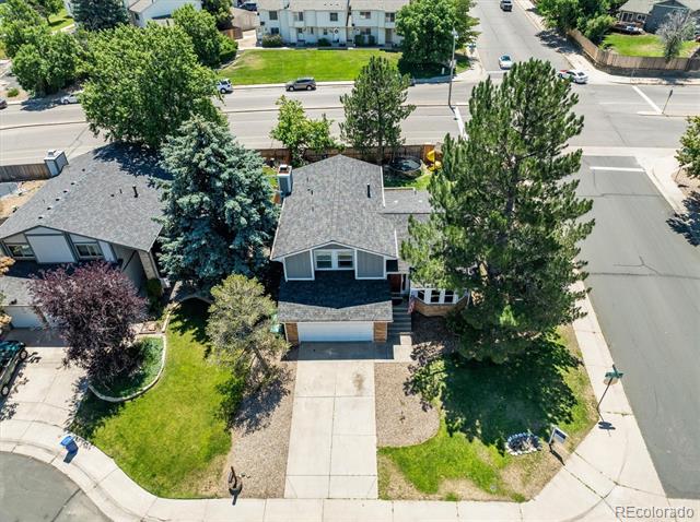 Single-story home with a gray roof, concrete driveway, front lawn, and mature trees.