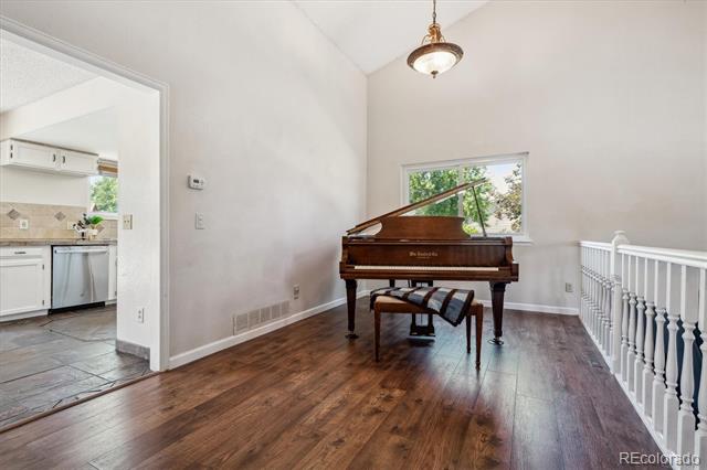 Upstairs room with a polished grand piano, hardwood floors, and a white stair railing.
