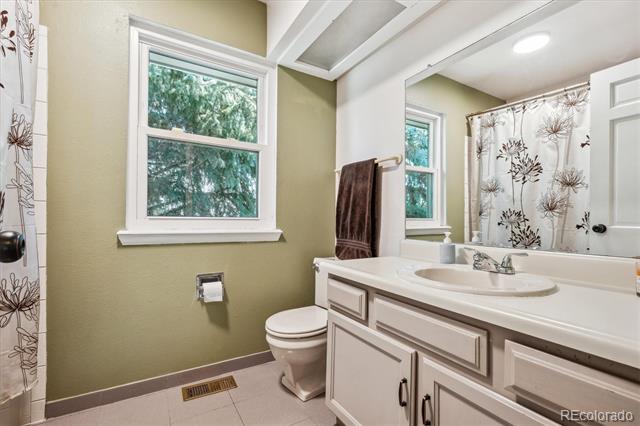 Bathroom with an olive-green wall, two windows, and a white vanity beside a floral-curtained tub.
