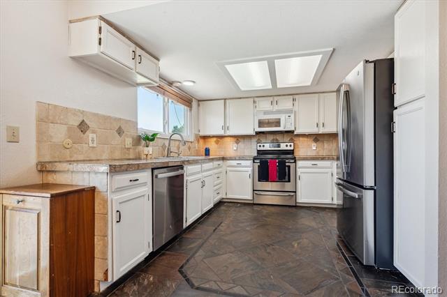 Kitchen with white cabinets, stainless steel appliances, and dark patterned tile flooring.