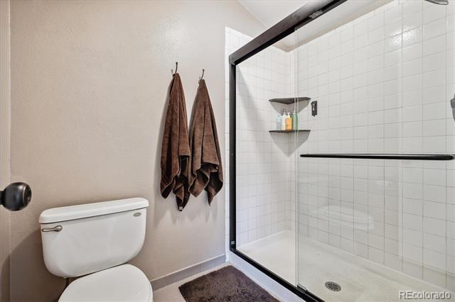 Bathroom with a black-framed glass shower, white tile, and brown towels.