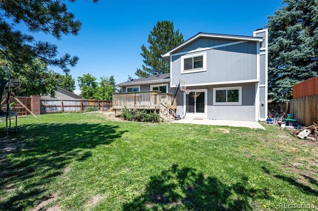 Rear exterior of a two-story gray home with a broad lawn, deck, and fenced yard.