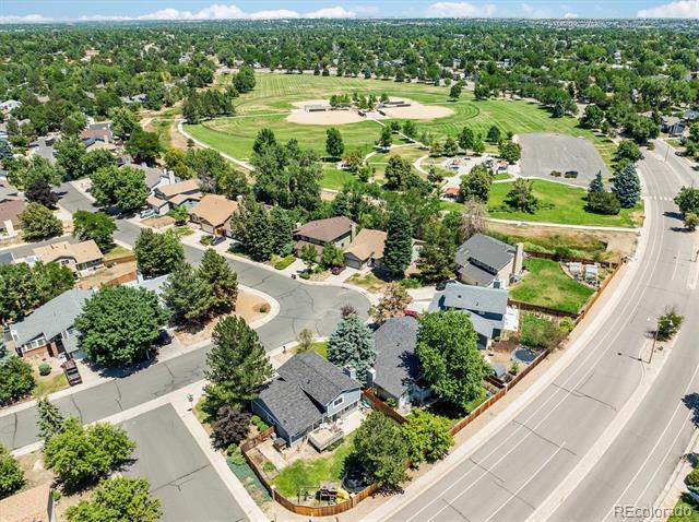 Aerial neighborhood view with tree-lined homes and a baseball field in the background.
