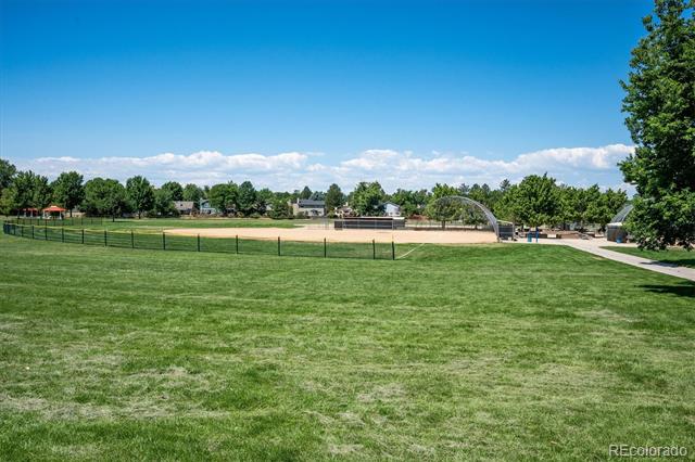 Grassy community sports field with a fenced baseball diamond beneath a clear blue sky.